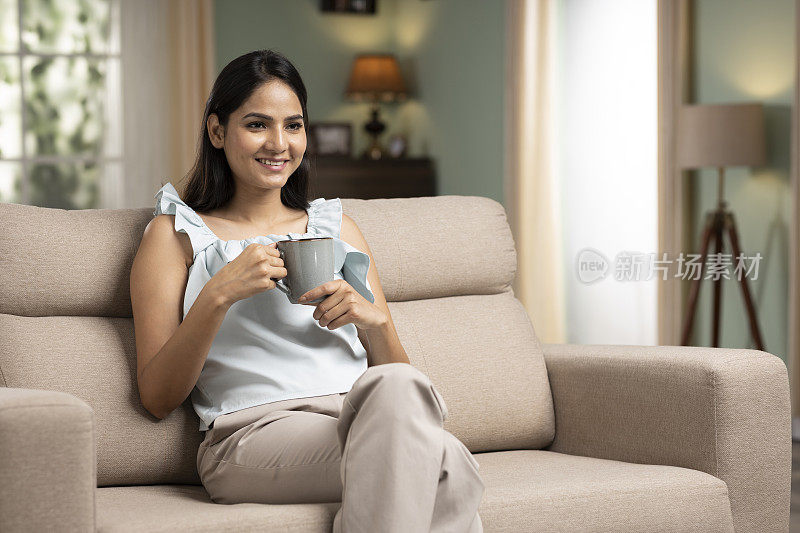 年轻女子坐在沙发上拿着喝咖啡，stock photo